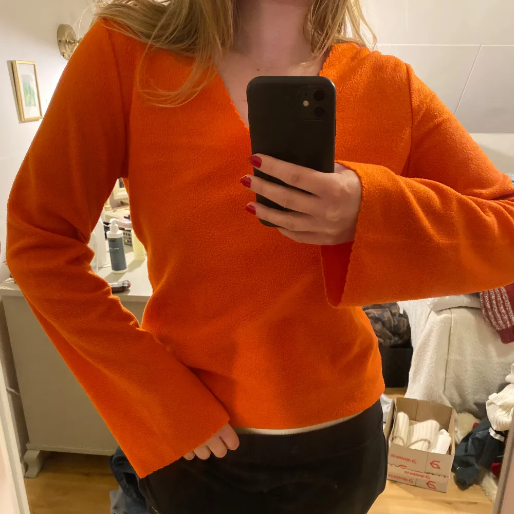 Säljer en snygg orange tröja i fleece med v-ringning och långa utsvängda ärmar. Från Vintage H&M. Har vågigt mönster längs med ärmarna. . Neuletakit & Villapaidat.