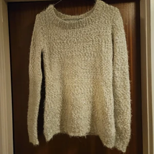Beige glittrig stickad tröja - Säljer en mysig beige stickad tröja med glittriga detaljer. Tröjan har långa ärmar och en rund halsringning. Perfekt för att lysa upp din garderob med lite glitter!