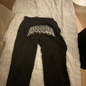 Svarta hoodrich byxor - Svarta mjukisbyxor med ett stort vitt tryck framtill. Byxorna har en avslappnad passform och är perfekta för en bekväm stil. De är gjorda i ett mjukt material som känns skönt mot huden.