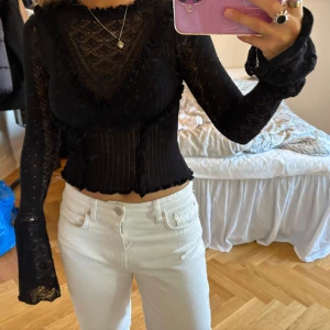 Svart spetsblus med volangdetaljer - Säljer en svart långärmad blus i spets med volangdetaljer och transparenta partier. Blusen har rund halsringning och vågiga kanter vid ärmslut och nederkant. 