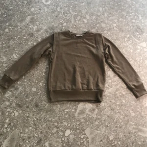 Olivgrön sweatshirt från Name It - Säljer en olivgrön sweatshirt från Name It. Tröjan har rund halsringning, långa ärmar och ribbade muddar vid ärmslut och nederkant. Perfekt för en avslappnad och stilren look.