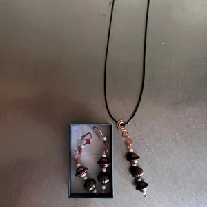 Svart och kopparfärgat smyckeset med halsband och örhängen - Säljer ett matchande smyckeset med halsband och örhängen. Båda har svarta och kopparfärgade pärlor i olika former, med detaljer i metall och ett svart snöre till halsbandet. Perfekt för dig som vill ha ett unikt set!