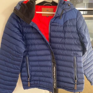 Blå dunjacka från Jackson Hole Originals -  Snake River Down Jacket från Jackson Hole Originals är en lätt dunjacka unisex som fungerar året runt, som ytterplagg eller som mellanlager under skaljacka. Lättvikt med axelpartierna i kraftigare material och 600+ fill power gåsdun. Formidabel passform, bra detaljer, populär även bland hästfolk. 900:-