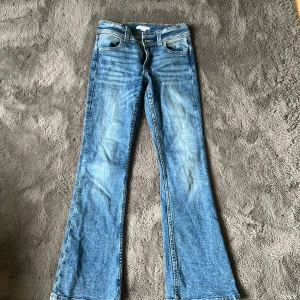 bootcut jeans  - Säljer ett par klassiska blå jeans från Gina Tricot i bootcut-modell. Jeansen har fyra fickor, normal passform och snygga slitningar framtill. Bakfickorna har dekorativ söm. Perfekta för dig som gillar en tidlös denimlook.