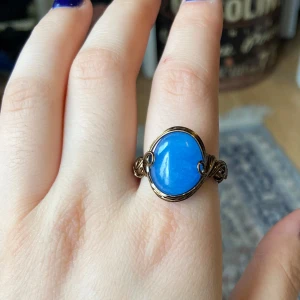 Ring med blå sten och metalltråd - Unik ring med en stor oval blå sten infattad i dekorativt lindad metalltråd. Ringen har en bohemisk känsla och den blå stenen ger ett färgstarkt intryck. Perfekt för dig som vill sticka ut med dina accessoarer.