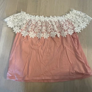 Rosa offshoulder topp med spets från H&M - Superfin rosa offshoulder topp från H&M med vit blommig spets upptill. Perfekt för varma dagar och ger en romantisk look med sina stora spetsblommor. Tunn och luftig modell.