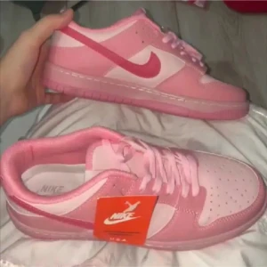 Rosa Nike Dunk sneakers - Snygga rosa Nike Dunk sneakers med vit sula och klassisk snörning. Perfekta för en sportig och trendig look. De har en rund tå och är tillverkade i syntetmaterial.
