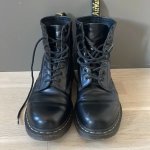 Svarta kängor från Dr. Martens - Säljer ett par klassiska svarta kängor från Dr. Martens med snörning och rund tå. De har den ikoniska gula sömmen och en slitstark sula. Perfekta för både stil och komfort.