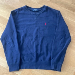 Mörkblå Ralph Lauren sweatshirt  - Säljer en snygg mörkblå tröja från Polo Ralph Lauren med det klassiska röda logotypbroderiet på bröstet. Perfekt för en stilren och avslappnad look. Tröjan är i storlek 14-16/160. Kom gärna med bud!