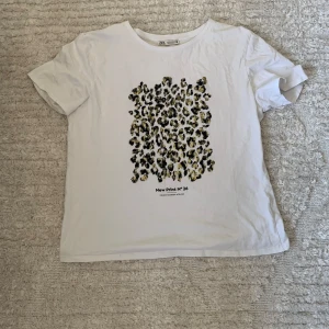 Vit t-shirt med leopardmönster från Zara - Vit t-shirt från Zara med ett stort leopardmönster i svart och gult på framsidan. Modellen har rund hals och korta ärmar. Säljer för den inte kommer till användning längre💕