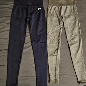 Två par seamless tights från Pursue Fitness - Säljer två par seamless tights från Pursue Fitness i storlek XS. Ett par är mörkblåa med diskret logga vid vristen, det andra paret är olivgröna med ribbade detaljer längs sidorna. Båda har hög midja och är perfekta för träning.