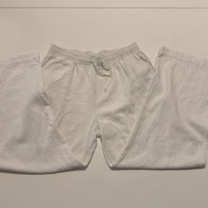 Vita linnebyxor - Säljer ett par vita linnebyxor med resår och snörning i midjan. Byxorna har rak passform och är tillverkade i ett tunt och luftigt linnematerial, perfekta för varma dagar.