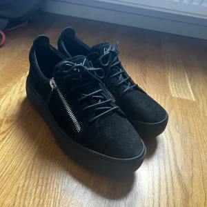  Giuseppe Zanotti - Säljer ett par svarta sneakers från Giuseppe Zanotti i mocka med snörning och silverfärgad dragkedja på sidorna. Skorna har en tjock, platt sula och rund tå. Perfekta för dig som gillar stilrena och exklusiva sneakers. Skicka dm om du har frågor eller vill ha fler bilder. Pris kan diskuteras vid snabb affär!