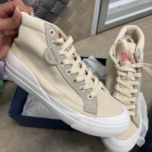 Beige sneakers från Levi's - Snygga beige sneakers från Levi's med högt skaft och vita sulor. Skorna har klassisk snörning och är tillverkade i canvasmaterial. Perfekta för en stilren och avslappnad look. Kommer i originalkartong.