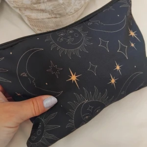 Necessär/Pennfodral/Sminkväska - En necessär/pennfack/sminkväska eller liknande, svart med gult mönster av solar, månar och stjärnor. Likadan på fram och baksida. Välfungerande dragkedja och ofodrad insida, ca 22×16 cm. Helt ny och oanvänd. 