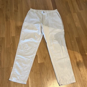 Beiga chinos från Uniqlo i linneblandning - Snygga beiga linne byxor från Uniqlo i en skön mix av bomull, linne och lite elastan för extra komfort. Klassisk rak passform med bälteshällor och knappstängning. Perfekta för en clean och avslappnad stil. Det är medium size och aldrig använda