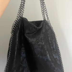 Svart axelväska med kedjedetaljer - Snygg svart axelväska med glansig yta och grova silverfärgade kedjor som handtag. Väskan har en mjuk, slouchy form, super fin men säljer då jag har två stycken!💕pris kan diskuteras 