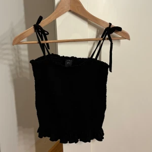 Svart smockad linnetopp från Lindex - Supersöt svart linnetopp från Lindex med smockad struktur och volangkant nertill.🤍