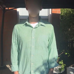 Grön- och vitrandig skjorta Ralph Lauren - Snygg grön- och vitrandig skjorta från Ralph Lauren. Skjortan är fitted, har klassisk krage, långa ärmar och knäppning framtill. Tillverkad i bomull och är non iron, vilket gör den enkel att sköta. Perfekt för dig som gillar stilrena och fräscha plagg. Skulle rekommendera dig som bär storlek M