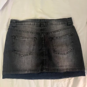 Svart jeanskjol med spetskant - Snygg svart jeanskjol från Brooker med klassisk femficksdesign och bälteshällor. Kjolen har en cool tvättad look och en fin spetskant längst ner som ger extra edge. Perfekt att matcha med sneakers eller boots för en chill vibe.