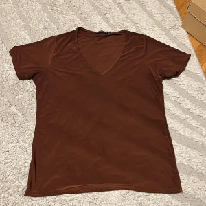 Brun v-ringad t-shirt - Snygg brun t-shirt med v-ringning och korta ärmar. Enkel och stilren modell som passar perfekt till jeans eller kjol. Materialet känns mjukt och följsamt mot huden.