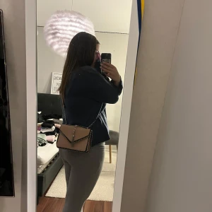 Ljus rosa axelväska med kedja och nitar - Säljer en ljus rosa axelväska med silverfärgad kedjerem och dekorativa nitar längs kanterna. Väskan har ett snyggt hängande tofsdetalj framtill och svarta kontrastkanter. Perfekt storlek för det viktigaste och flera fack inuti.