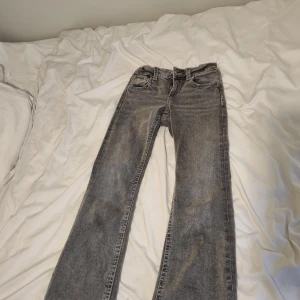 Grå jeans med raka ben - Säljer ett par grå bootcut jeans. Dem har snygga kontrastsömmar, samt detaljerade bakfickor med lock och knapp. Perfekta för dig som gillar en avslappnad och stilren look. 