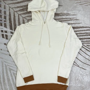 Vit hoodie med bruna muddar - Unik och bekväm hoodie som är handgjord. Färgen är offwhite med brun botten på både ärmarna och nederdelen av tröjan, vilket ger ett stilrent intryck. Passar perfekt att använda hemma eller som en snygg vardagsdetalj. Mjuk insida och skön passform för dig som gillar avslappnade plagg.   Storlek: S/M  Använd men i mycket fint skick! (Kan var felsydd).  