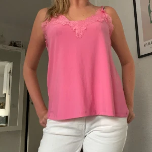 Rosa linnetopp med spetsdetaljer - Säljer en söt rosa linnetopp med tunna axelband och fina spetsdetaljer längs urringningen. Toppen har en lös passform och är perfekt för varma dagar. Materialet känns mjukt och lätt mot huden.