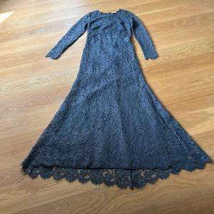 Mörkblå spetsklänning från Valerie - Långklänning i stålblå spets från Valerie med lång ärm och figurnära passform. Klänningen har vackra blommiga spetsdetaljer, rund halsringning och dragkedja i ryggen. Använd 1 gång.