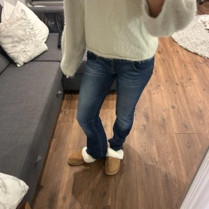 Blå bootcut jeans med låg midja - Säljer ett par klassiska blå jeans med bootcut-modell och låg midja. Jeansen har snygga slitningar framtill och femficksdesign. Perfekta för dig som gillar en tidlös och avslappnad look. Materialet är jeans och passformen är normal. Är 174 för referens!