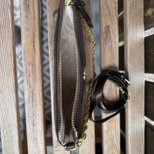 Gucci axelväska med kedja och GG-mönster - Snygg axelväska från Gucci med klassiskt GG-mönster i beige och brunt. Väskan har guldfärgad kedja, bruna skinn-detaljer och dragkedja upptill. Perfekt storlek för det viktigaste och ger en lyxig touch till din outfit.