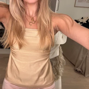 Champagnefärgad bandeau tubtopp - Säljer en snygg champagnefärgad bandeau tubtopp i glansigt satinliknande material. Toppen är axelbandslös och har en stilren, enkel design som sitter tight över bysten och faller lite lösare nedtill✨✨Storleken är okänd men skulle gissa på xs/s