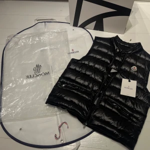Moncler väst - Tja, nu säljer vi denna as snygga moncler väst!!!  •Inga defekter •Två ägare •Finns kvitto + NFC Tag •Orginal påse + Tag    Storlek: 2 vilket är ungefär S och uppåt/ modellen på bilden är 173cm Modellen är efter 2021, vilket innebär att den klassiska äktehets verifieringen via industri logan inte finns, då det endast fanns mellan 2013-2020.  Ny pris :-9,899kr idag🤑 Vårt pris 3999kr🤯💛 Perfekt till dig som vill ha något alldeles extra till skolstarten!!!🤩🤩🤩 Skriv vid minsta fundering!!!