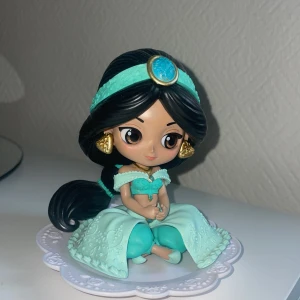 Prinsessan Jasmin  - Bilderna visar en söt figur i turkos klänning och smycken, sittande på ett dekorativt fat. Figuren har långt svart hår med turkosa detaljer och guldörhängen. Perfekt för dig som gillar samlarprylar eller vill ha en cool dekoration till rummet.