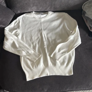 Vit stickad tröja från Zara - Klassisk vit stickad tröja från Zara med rund halsringning och ribbade muddar vid ärmslut och nederkant. Tröjan har en clean och enkel look som passar perfekt till jeans eller kjol. Materialet är mjukt och skönt mot huden.