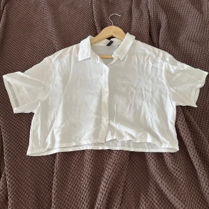 Vit croppad skjorta  - Snygg vit skjorta med kort ärm och croppad passform. Skjortan har klassisk krage, knäppning framtill och är tillverkad i ett lätt och luftigt material som känns skönt mot huden.