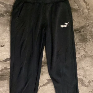 Svarta mjukisbyxor från Puma - Svarta mjukisbyxor från Puma med vit logga på vänster lår. Byxorna har resår i midjan och sidofickor, perfekta för chill eller träning. Tillverkade i mjukt och bekvämt material. Är en storlek L men sitter även på som en M.