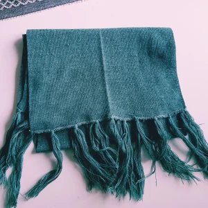 Grön stickad halsduk med fransar - En stilren grön halsduk med långa fransar i ändarna. Halsduken är stickad och har en mjuk känsla, perfekt att svepa runt halsen när det är kyligt ute. Enkel design som passar till många olika outfits.  Helt skick dock lite tråddragning & obehandlad fläck