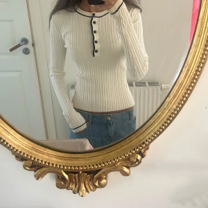 Vit ribbad långärmad tröja med knappar - Supersnygg vit ribbad tröja med svarta detaljer och knappar framtill. Långärmad och tight passform som framhäver figuren. Perfekt till jeans eller kjol för en clean och stilren look.