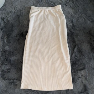 Beige ribbad långkjol - Säljer en beige långkjol med ribbad struktur. Kjolen har rak passform och resår i midjan för extra komfort. Perfekt för dig som gillar en clean och stilren look. Materialet känns mjukt och följsamt.