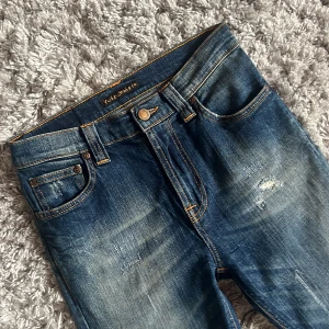 Nudie jeans med slitningar - Säljer dessa riktigt snygga Nudie jeansen med slitningar. De är i modellen High Kai och är i riktigt bra skick, inga defekter. Storleken är W28 L32. Bara att skriva över frågor och funderingar.