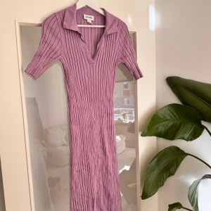 Lila ribbad klänning från Monki - Superfin strechig,  lila ribbad klänning från Monki med v-ringning och krage. Klänningen är figurnära, har korta ärmar och är i en mjuk stickad bomullsblandning. Perfekt för vår och sommar när du vill vara både bekväm och snygg. Klänningen är i jättebra skick då jag enbart använt den fåtal gånger