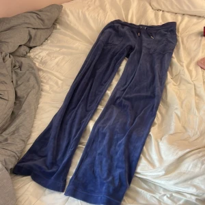  Juicy Couture byxor - Mysiga blåa velourbyxor från Juicy Couture med broderad JC-logga på benet och snörning i midjan med metalländar. Byxorna har en loose passform och bootcut-ben, perfekta för en chill och trendig look.