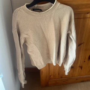 Beige stickad tröja från KappAhl XS - Beige stickad tröja från KappAhl i storlek XS. Tröjan har en grovstickad struktur, rund halsringning och ribbade muddar vid ärmslut och nederkant. Perfekt för lager-på-lager och enkel att matcha med jeans eller kjol.