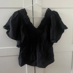 Svart blus med voluminösa ärmar Lindex XS - Supersnygg svart blus från Lindex i storlek XS. Blusen har en djup v-ringning med rynkade detaljer och stora, voluminösa korta ärmar som ger en trendig siluett. Perfekt för dig som vill sticka ut med en cool och luftig topp.