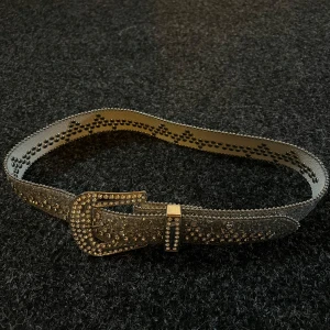 Glittrigt silverbälte med strassdetaljer - Säljer ett riktigt snyggt bälte i silver med massor av glittriga strass och stenar över hela bandet och spännet. Bältet har en klassisk form med markerad kant och ett rejält spänne som också är täckt av stenar. Perfekt för att lyfta vilken outfit som helst.🩶🪩