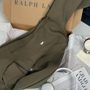 Olivgrön hoodie från Polo Ralph Lauren - Säljer en olivgrön hoodie från Polo Ralph Lauren med dragkedja och klassisk vit broderad logga på bröstet. Tröjan har huva, långa ärmar och ribbade muddar. Perfekt för en chill och stilren look. Storlek M men passar S. Sälja pga att den ej passar…