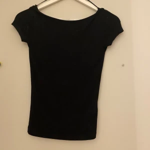 Svart tight topp med öppen rygg från Gina Tricot XS - Svart, tight topp från Gina Tricot i storlek XS. T-shirtrmodell med korta ärmar och en djup, rundad rygg som ger en snygg och stilren look. Perfekt att styla med jeans eller kjol för en clean vibe.