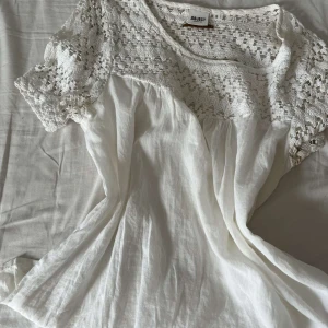 Vit spetsblus från Object - Supersöt vit blus från Object med virkade spetsdetaljer upptill och på ärmarna. Blusen har korta ärmar och en luftig, flowy passform. Perfekt för dig som gillar romantisk och bohemisk stil. Materialet känns lätt och somrigt.